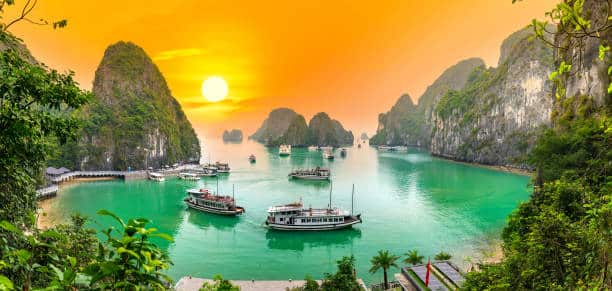 Karsts calcaires et eaux turquoise de la baie d’Halong sous un coucher de soleil coloré.