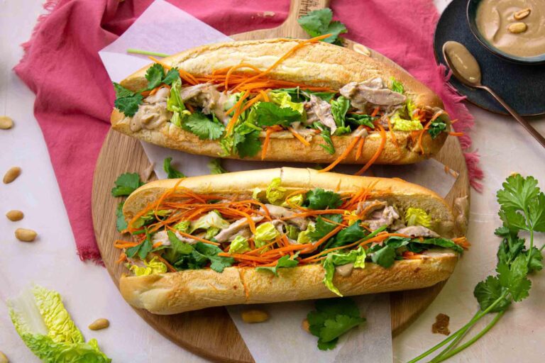 Un bánh mì croustillant garni de légumes, viande et sauces dans une assiette en bois.