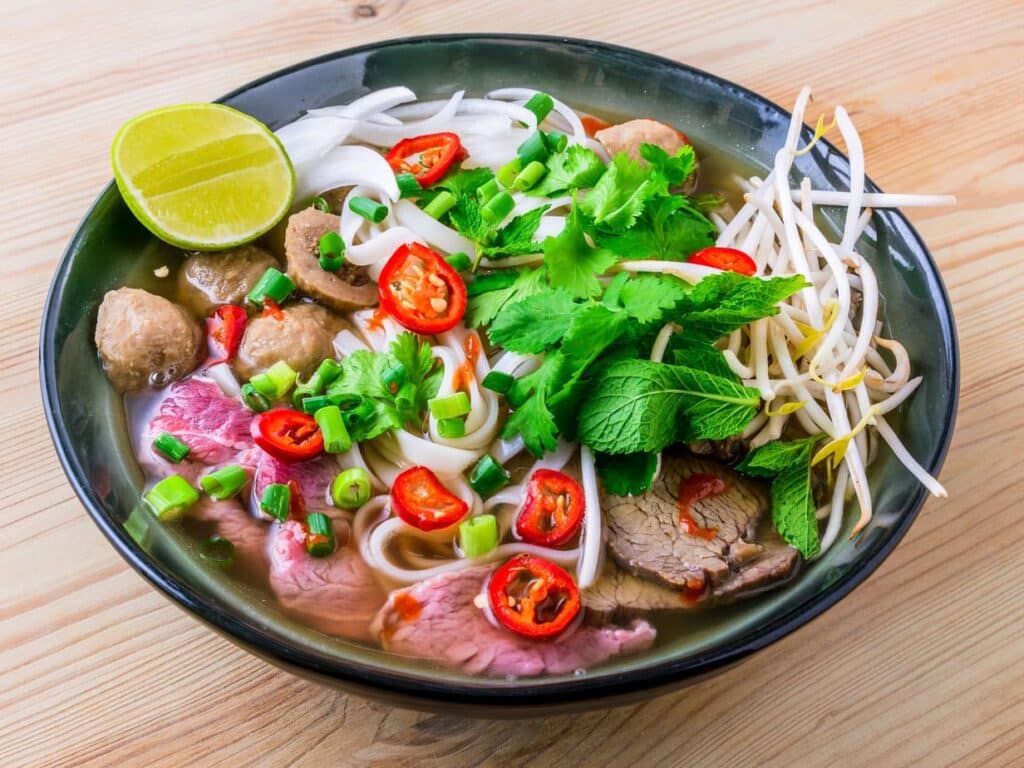 Un bol fumant de phở garni de citron vert, de coriandre et de piment.